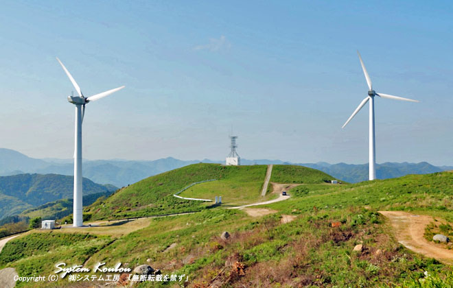 広い草原の千俵蒔山（せんびょうまきやま）の山頂。風力発電の風車が２基建っている