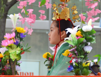桟敷台に乗る舞姫の少女は少女は天冠をかぶり舞衣に赤い緋袴(ひのはかま)姿